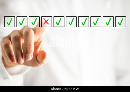 Man selecting a red cross in a box from a line of green check marks or ticks in boxes on a virtual screen conceptual of individuality, quality, failur Stock Photo