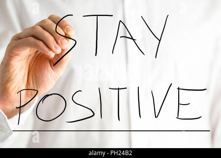 Closeup of the hand of a man wearing a white shirt writing - Stay Positive - on a virtual screen. Concept of optimism. Stock Photo