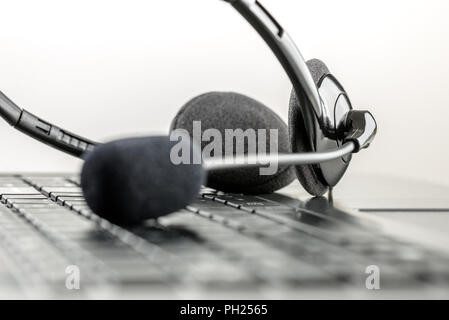 Monochrome black and white image of a headset lying on a laptop computer keyboard conceptual of telemarketing, call center, client services or online  Stock Photo