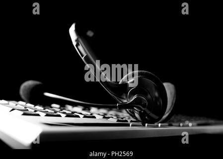 Low angle conceptual black and white image of a headset lying on a computer keyboard against a dark background with copyspace depicting a call centre, Stock Photo