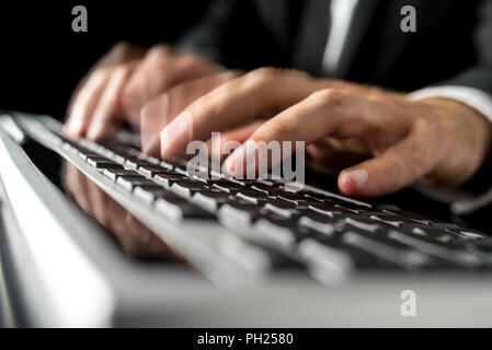 Close-up with motion blur effect of the hands of a man wearing business suit while typing fast on a desktop computer black keyboard. Stock Photo