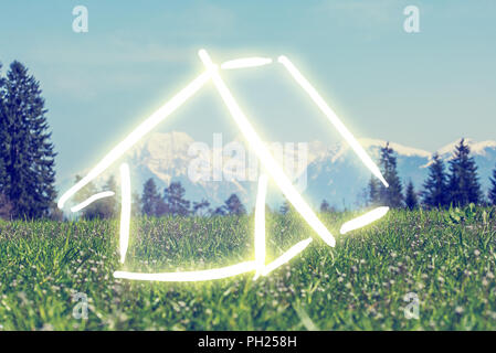 Hand-drawn house in white on a green field against a backdrop of a scenic mountain landscape, conceptual of a dream eco house and ownership. Stock Photo
