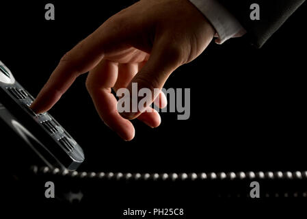 Close-up of the hand of a businessman dialing or initiating a phone call by operating the keypad of a desk corded land line telephone, on black. Stock Photo