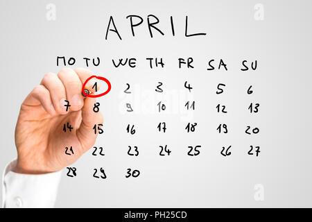 Hand drawn calendar for April on a virtual interface or screen with the First ringed in red by a man holding a marker pen, closeup of his hand. Fools  Stock Photo