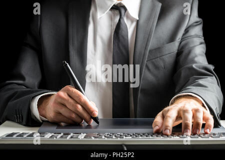 Front view of male graphic designer or photographer  in an elegant suit sitting at his office desk working with stylus pen on digital tablet and simul Stock Photo