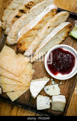 rustic mixed cheese board platter with toasted bread and redcurrant jam on wooden tray Stock Photo