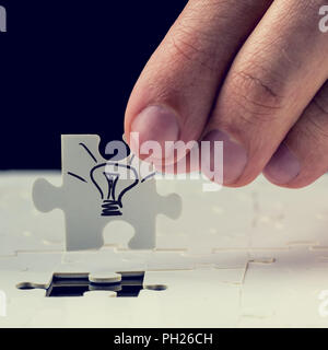 Male hand inserting the final missing puzzle piece with light bulb drawn on it. Concept of innovation or getting a business idea. Stock Photo