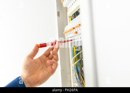Electrician testing an electrical circuit board with a handheld tester to determine if there is current and voltage during repairs or installation of  Stock Photo