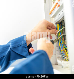 Electrician installing an electrical fuse box in a house working with pliers on the wiring circuits Stock Photo