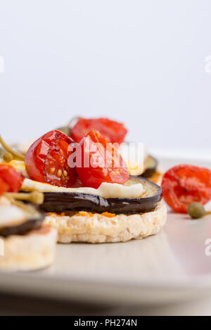 Delicious Italian appetizer of corn cracker topped with baked egg and juicy grilled aubergine and cherry tomatoes. Stock Photo