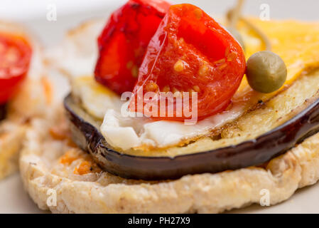 Closeup of Italian appetizer of corn cracker topped with baked egg and juicy grilled aubergine and cherry tomatoes. Stock Photo