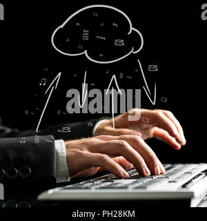 Businessman typing on the keyboard of his computer synchronizing files with the cloud storage with a hand-drawn cloud icon with data transfer arrows. Stock Photo