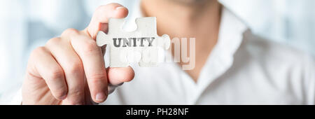 Businessman Showing a Conceptual White Jigsaw Puzzle Piece with Unity Text in Close up. Stock Photo
