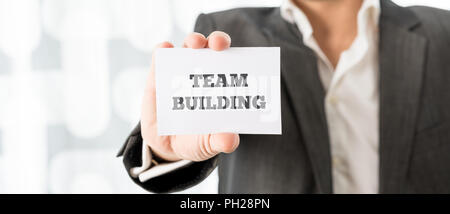 Close up Businessman Showing a Conceptual Small White Card with Team Building Texts on a Blurred Abstract Background. Stock Photo