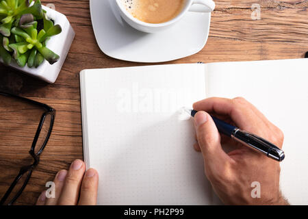 Close-up Of A Person Writing On Notebook Over Wooden Desk Stock Photo