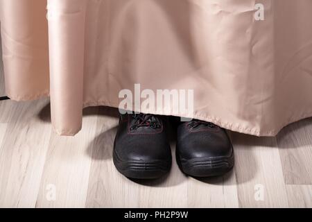View Of A Person Shoe's Hiding Behind Curtain Stock Photo