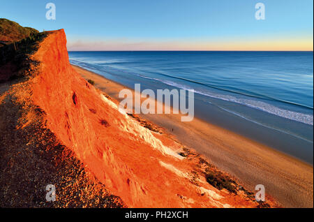 Scenic evening atmosphere at long sand beach with red sand cliffs and calm ocean Stock Photo