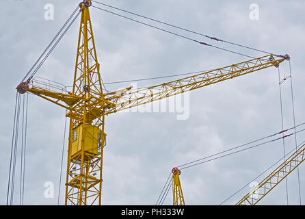 Two yellow construction crans on the cloudy sky background, the view from the bottom up. Stock Photo