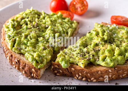 Close up of a slice of delicious avocado toast with sliced tomato. Stock Photo