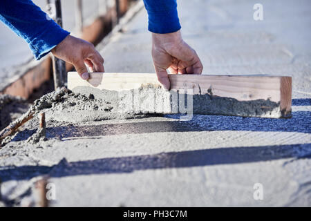 The hands of a mason using a piece of wood to level and move wet cement on a newly poured slab Stock Photo