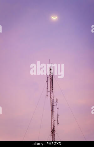 View of the moon on the dusk sky and the folded dipole radio antenna for telecommunications with colorful sky background. Silhouette amateur radio ant Stock Photo
