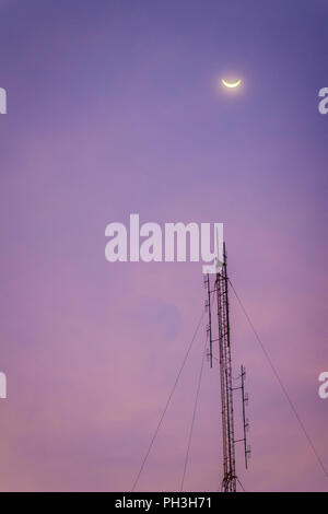 View of the moon on the dusk sky and the folded dipole radio antenna for telecommunications with colorful sky background. Silhouette amateur radio ant Stock Photo
