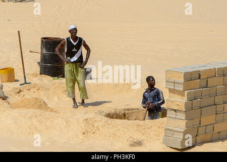 KAYAR, SENEGAL - APR 27, 2017: Unidentified Senegalese man digs a hole near the heap of bricks in a beautiful village near Kayar, Senegal Stock Photo