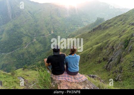 Couple travelers Man and Woman sitting on cliff, relaxing. Mountains aerial view Stock Photo