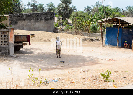ROAD TO BISSAU, GUINEA B. - MAY 1, 2017: Unidentified local woman stands in the middle of the street in a village in Guinea Bissau. Still many people  Stock Photo