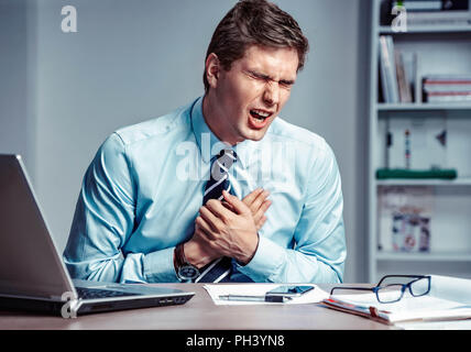 Office manager having heart attack. Photo of young man holding hand on painful chest in the workplace. Medical concept. Stock Photo