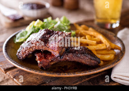 A plate of delicious barbecued ribs with french fries and salad. Stock Photo