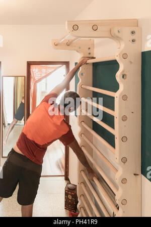 61 year old man exercising at home on homemade wall bars in small apartment.
