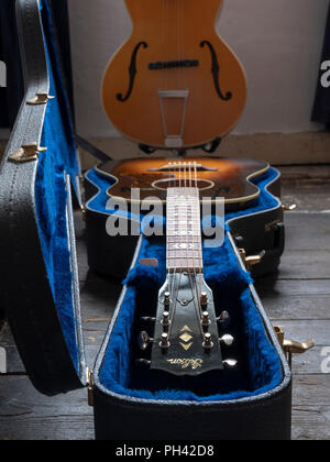Gibson J-45 acoustic guitar in its case with a blond semi-acoustic f hole archtop guitar in the background. Stock Photo