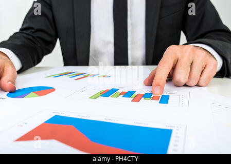 Businessman analysing a set of bar graphs as he sits at his desk pointing to one column chart, in a business analysis, projections and strategy concep Stock Photo