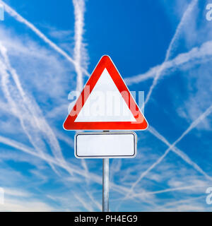 Blank white triangular traffic warning sign on a signpost against a sunny blue sky with crisis-crossing contrails from jetliners with copyspace for yo Stock Photo
