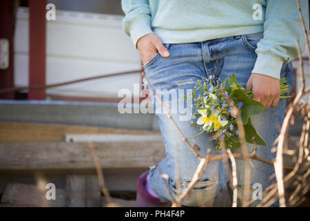Young woman on blue jeans holding a beautiful garden flowers in her hand. Summer bouquet in girl's hand. Outdoor. Spring garden present. Sunlight in t Stock Photo