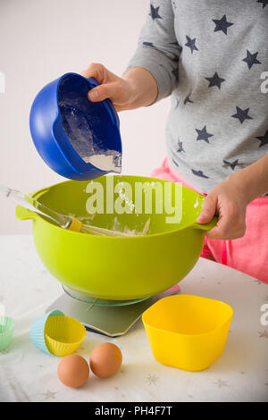 Woman making dough for muffins. Mixing flour, sugar, eggs and other ingredients from colorful bowls. Homemade food, baking at home. Stock Photo