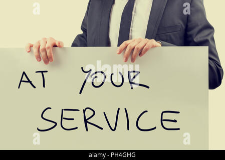 Businessman holding white signboard with Aty your service sign handwritten on it. Stock Photo