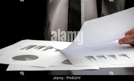 Close up of the hands of a businessman seated at his desk analysing a set of statistic report and holding a spreadsheet with graphs in his hand. Stock Photo