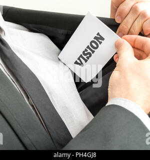 Businessman removing or placing a white card with word Vision in the inner pocket of his suit jacket. Stock Photo