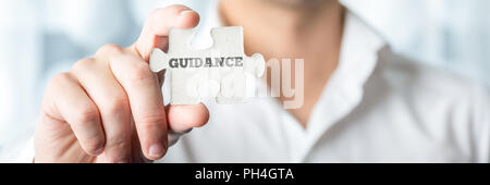 Close up Businessman Hand Holding Puzzle Piece with Conceptual Guidance Text In Front of the Camera. Stock Photo