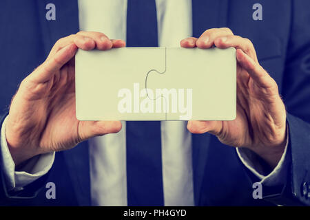 Businessman holding two blank white interlocked puzzle pieces with copyspace for your text conceptual of teamwork, problem solving or meeting a busine Stock Photo