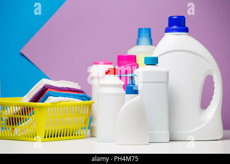 Photo of several bottles of detergents and multi-colored towels in basket isolated on purple, blue background Stock Photo