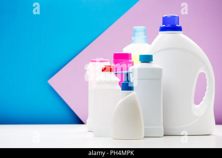 Photo of bottles of cleaning products on white table isolated on blue , purple background Stock Photo