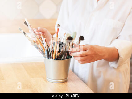 Different brushes in metal bucket with artist hands, selective focus Stock Photo