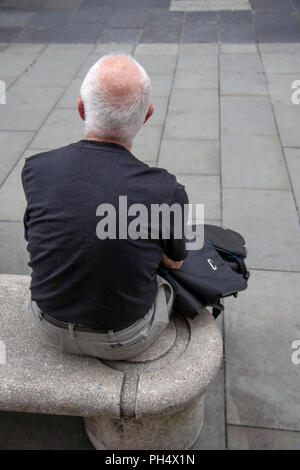 Senior man facing away sitting on a public stone bench in High Street, Sheffield, South Yorkshire, England Stock Photo