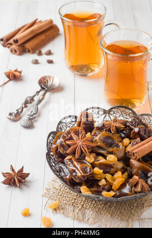 Oriental sweets, dried fruit dates and raisins, cinnamon and star anise in a plate. Turkish tea in glasses on a wooden background Stock Photo