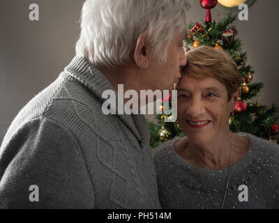 Closeup protrait of an elderly couple kissing in front of a Christmas tree Stock Photo