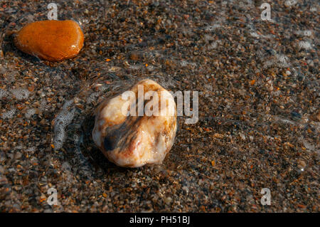 two small wet pebbles near the shoreline partially immersed in the water