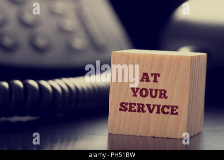At Your Service written on a wooden cube in front of a telephone conceptual of help, client services, assistance, expertise and consultancy. Stock Photo